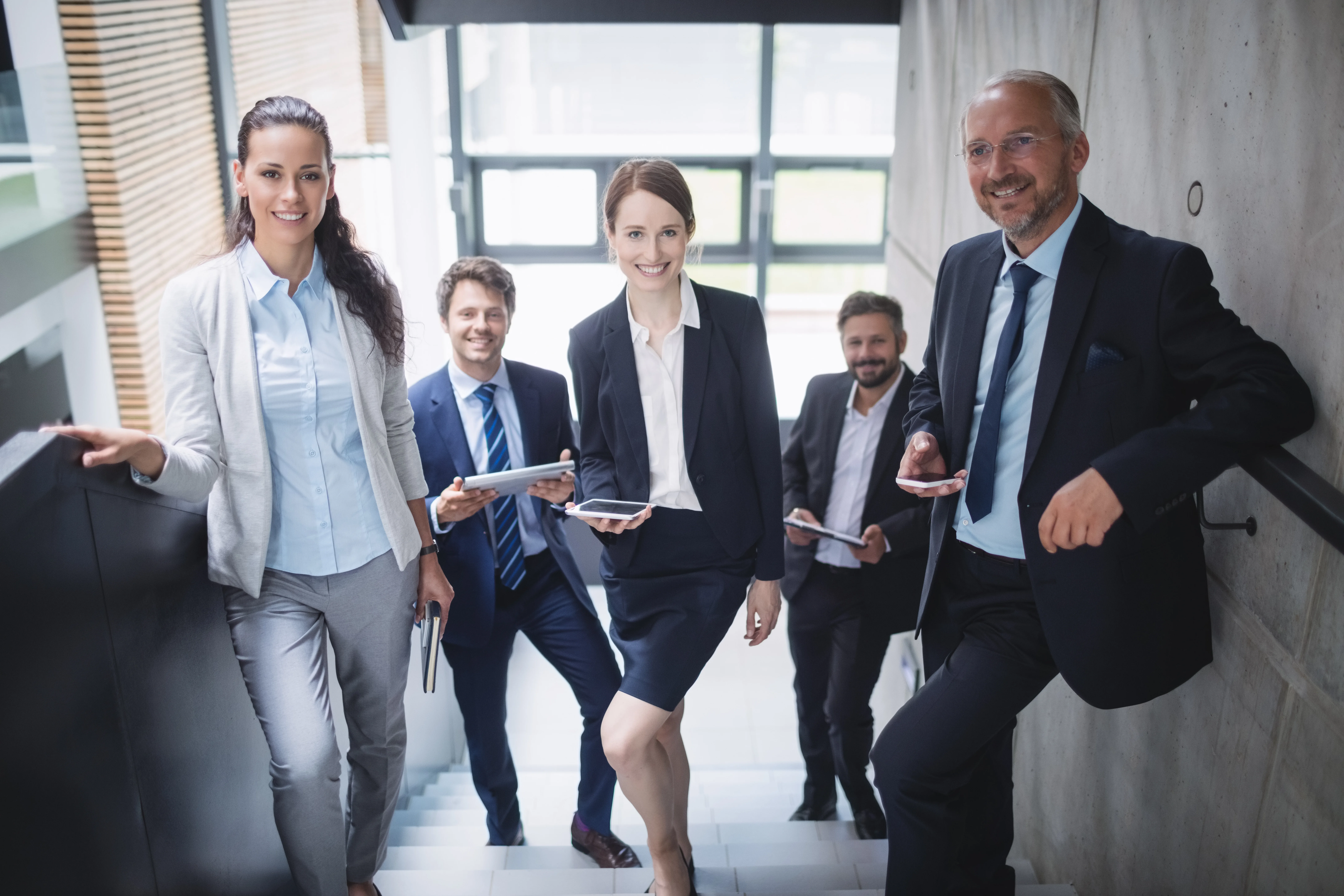 A group of business professionals standing together in front of a modern office building. They are smiling and looking at the camera.